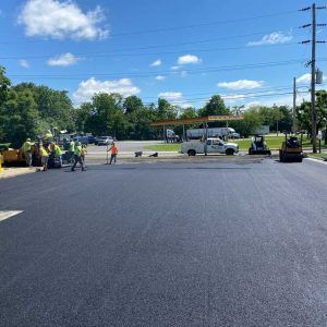 Road construction crew working beside a paved road under a blue sky, with trucks and equipment nearby