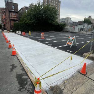 Freshly poured concrete sidewalk ramp beside a parking lot, marked off with cones and caution tape