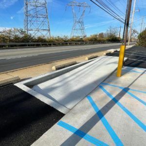 Raised sidewalk ramp beside a road, marked with blue tape near utility poles under a clear sky
