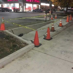 Orange cones and caution tape block a damaged parking lot area near a storefront at night