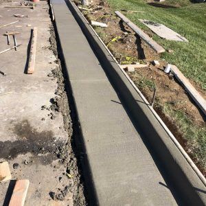 Fresh concrete curb along a narrow trench beside a partially dug sidewalk and grass