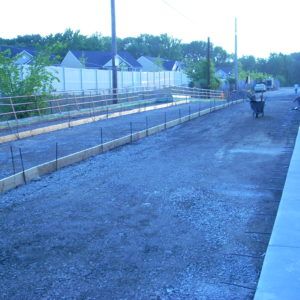 Gravel path beside train tracks with a few people in the distance, viewed along a residential fence line.