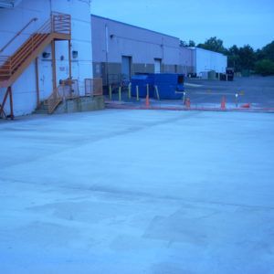 Blue-tinted warehouse loading area with stairs, cones, and a fenced-off section at dusk