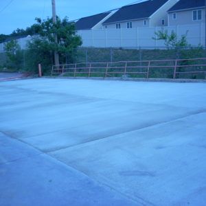 Empty concrete parking lot beside a fence and houses at dusk