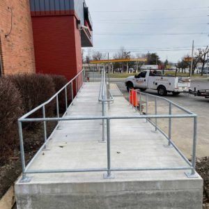 Ramped walkway with metal railings beside a brick building, leading to a parking lot with a white truck.