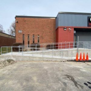 Brick building entrance with wheelchair ramp, railings, and orange cones outside