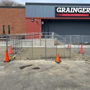 Construction barricade and orange cones blocking a cracked parking lot outside a Grainger store entrance