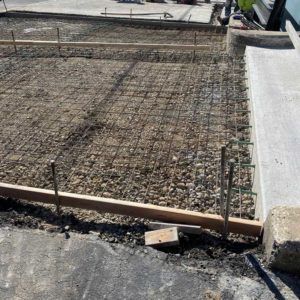 Construction site with rebar grid and concrete foundation forms beside a white wall