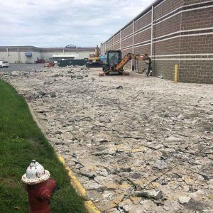 Construction site with excavator beside a brick wall and rough demolished pavement, with a fire hydrant in foreground