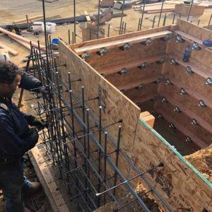 Workers building a concrete foundation with rebar and wooden formwork at a construction site