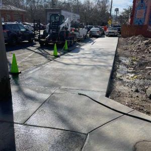 Freshly poured sidewalk beside parked cars, with orange cones marking a closed path.