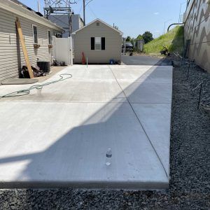 Concrete driveway between a house and retaining wall, with a small shed at the back.