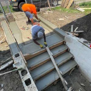 Workers pouring concrete on a stairway construction site, with forms and tools around them