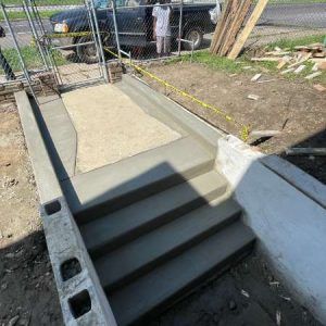 Concrete wheelchair ramp with handrails and steps at a construction site, viewed from above.