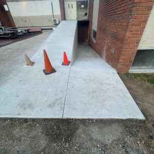 Concrete ramp beside a brick building with three traffic cones blocking the lower entrance path