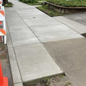 New concrete sidewalk with a curb ramp beside orange construction barricades