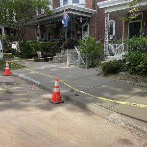 Sidewalk blocked off with caution tape and orange cones outside brick homes after storm damage