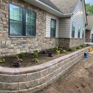 Stone-edged garden bed beside a house with newly planted shrubs and fresh mulch