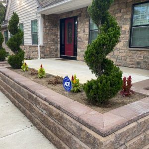 Front porch with stone house, red door, trimmed shrubs, and an ADT security sign.