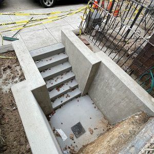 Concrete basement stairwell beside construction site, with yellow caution tape and exposed rebar.