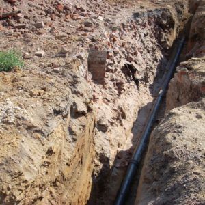 Black pipe laid in a narrow dirt trench at a construction site