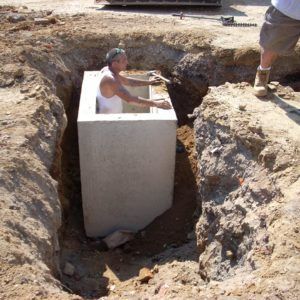 Man in a large white container being lowered into a dug-out trench at a construction site