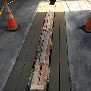 Construction trench covered with wooden planks between orange safety cones on concrete