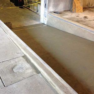 Concrete curb ramp with a smooth sloped walkway beside steps in an indoor construction area