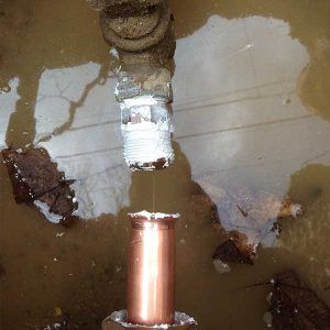 Copper pipe emerging from muddy water, connected to a taped joint and metal fitting.