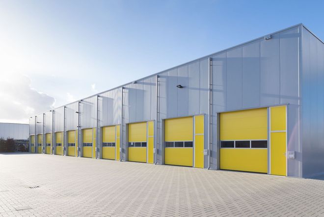 Modern industrial warehouse with yellow loading bay doors on a snowy lot under a clear sky