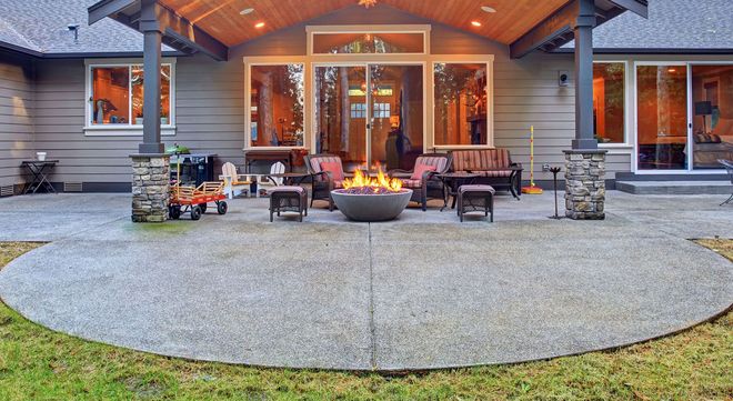 Outdoor patio with modern fire pit, seating, and stone columns in front of a house
