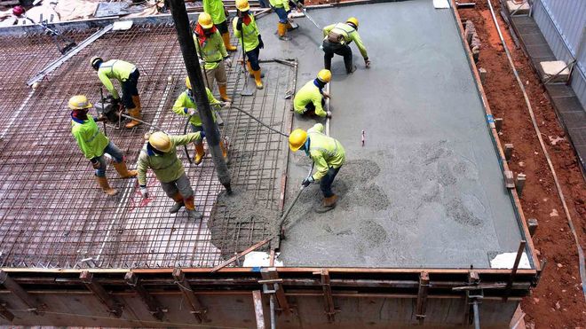 Construction workers pour and smooth concrete on a building rooftop slab.