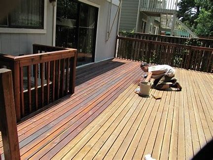 a man is kneeling on a wooden deck painting it