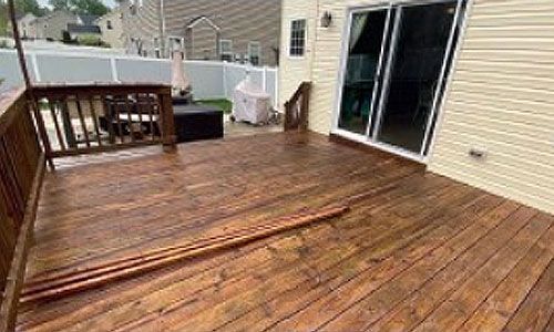 Wooden deck with brown stain, next to a house with sliding glass doors. Copper pipes lie on the deck.