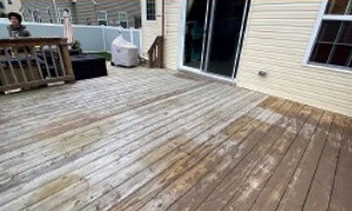 Wooden deck being cleaned. Partially cleaned boards are brown, while the untouched areas are faded.