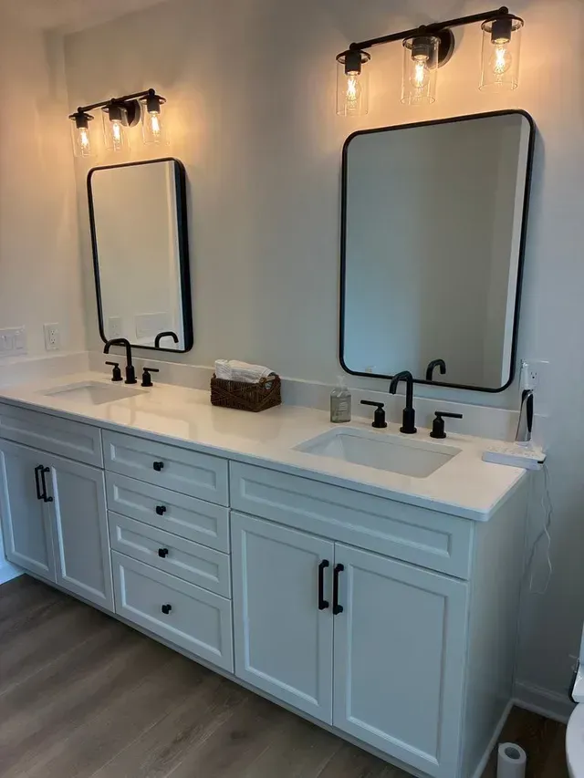 Double vanity bathroom with white cabinets, black faucets, lit sconces, and two mirrors
