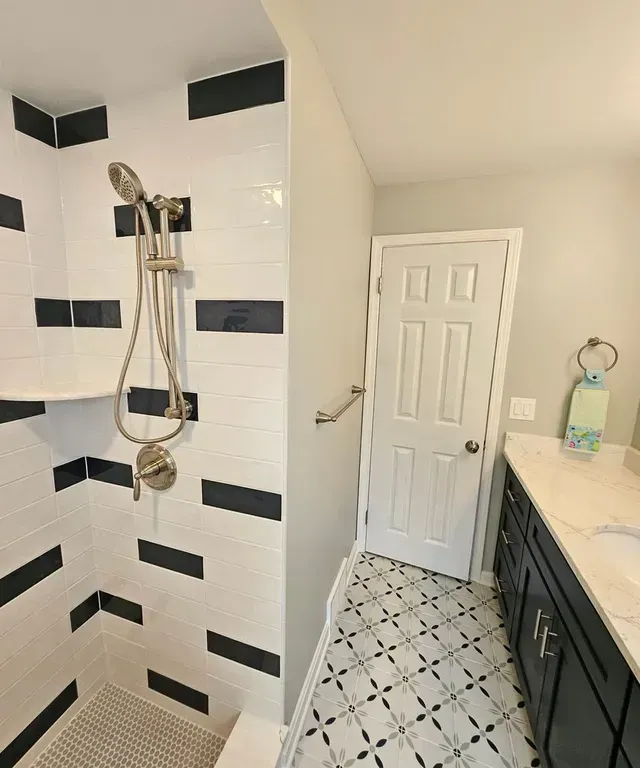 Bathroom with black-and-white tile shower, white door, and vanity with countertop toiletries.
