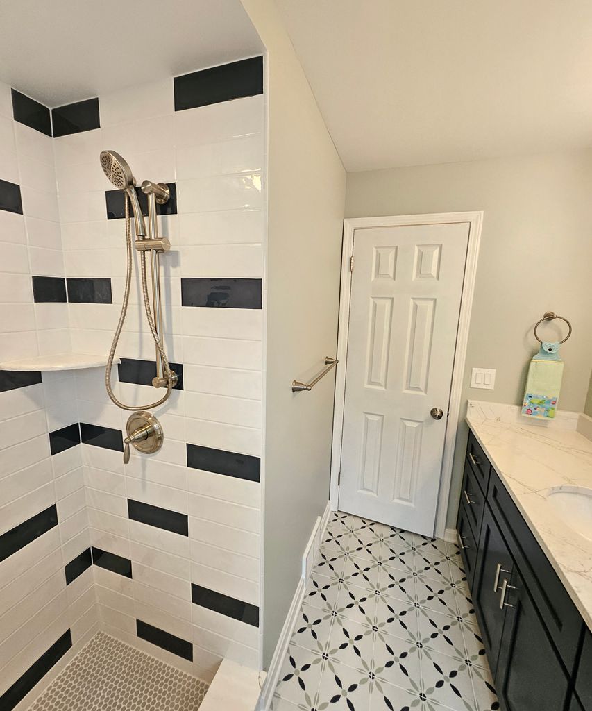 Bathroom with black-and-white tile shower, white door, and dark vanity sink.