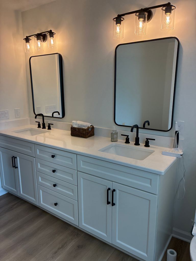 Double vanity bathroom with two framed mirrors, black fixtures, and white cabinets under wall sconces