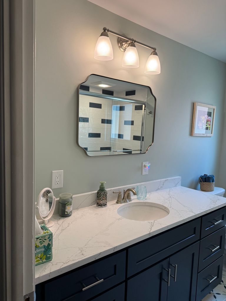 Bathroom vanity with black cabinets, white countertop, and mirror under three lights