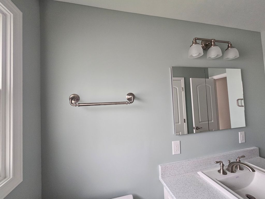 Bathroom vanity with light gray walls, mirror, towel bar, and three-bulb light fixture above the sink.