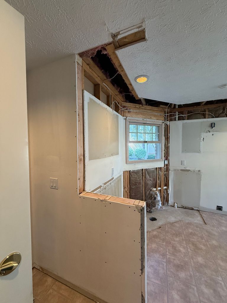 Partially demolished interior room with exposed studs, broken ceiling, and a window visible through the wall opening
