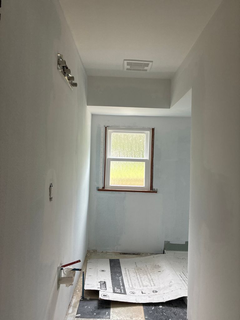 Narrow white hallway under renovation with a window at the end and construction materials on the floor