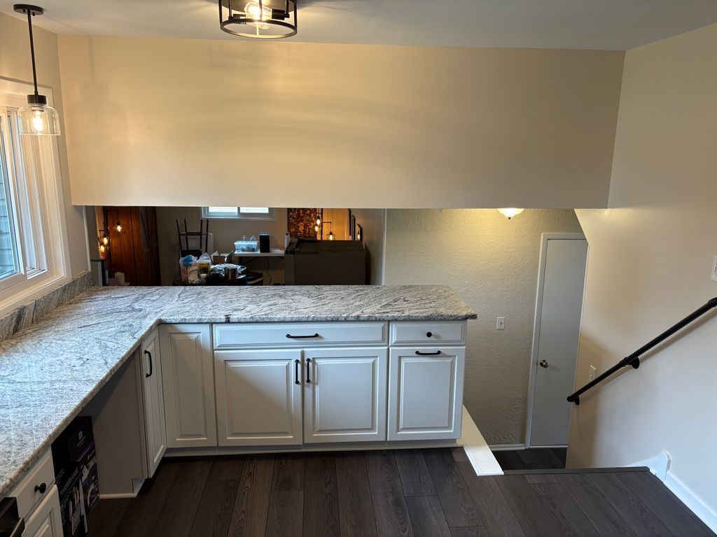 Bright kitchen with white cabinets, speckled countertop, and a stairway on the right