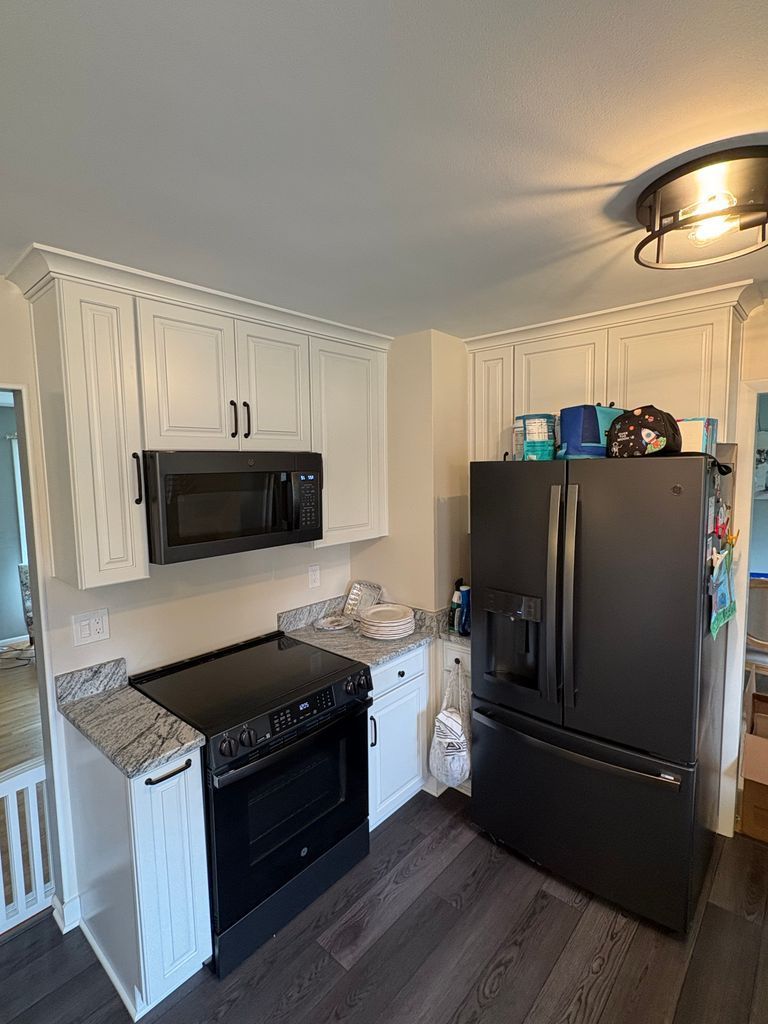 Small kitchen with white cabinets, black stove and refrigerator, and dark wood flooring.