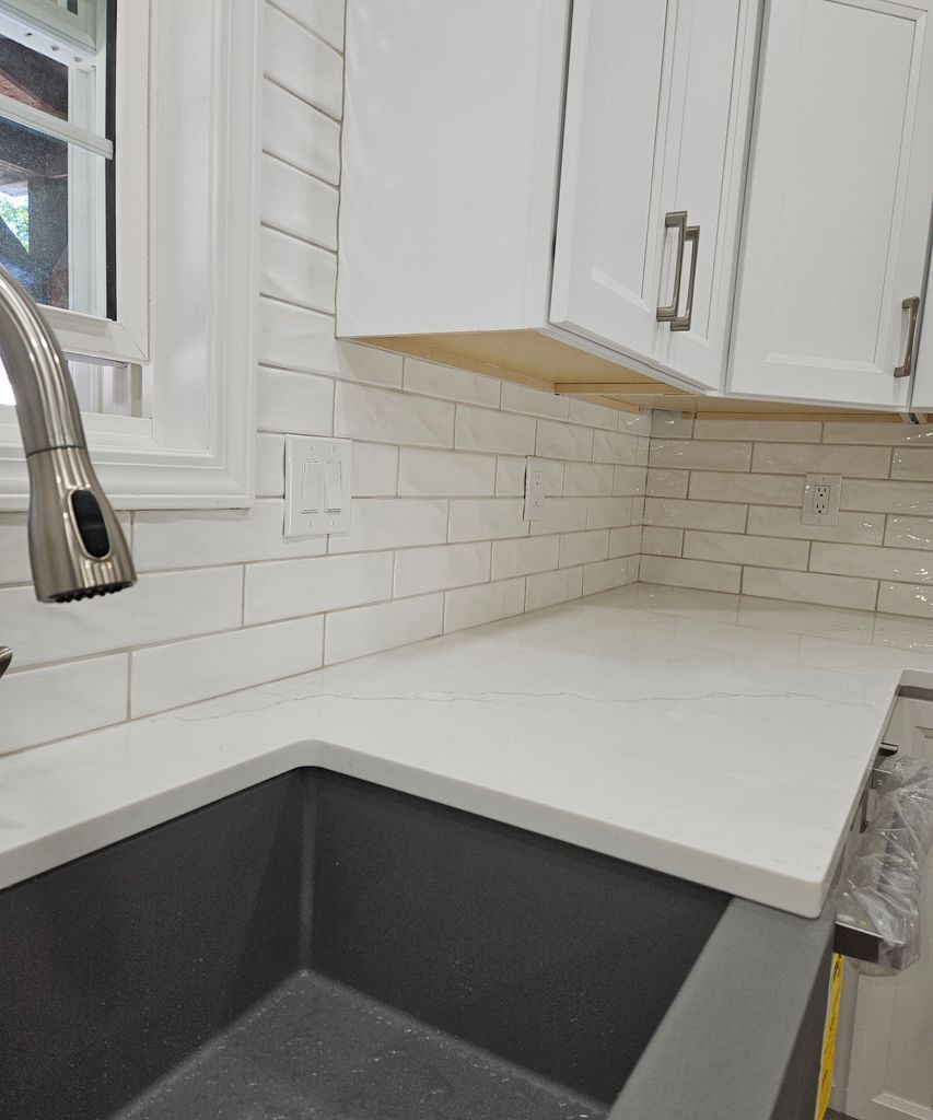 White kitchen countertop beside a black sink, with white subway tile backsplash and cabinets