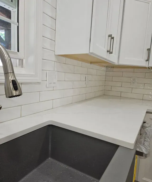 Modern kitchen corner with white cabinets, white subway tile, and a black sink by a window