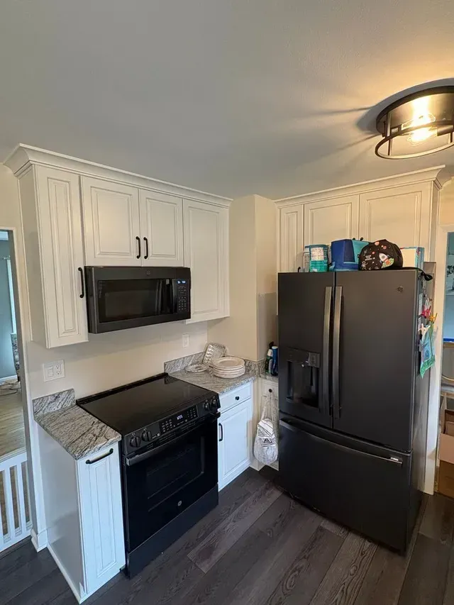 Small kitchen with black appliances, white cabinets, speckled countertops, and dark wood flooring.