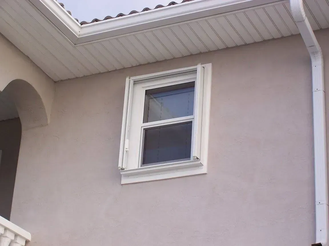 White-framed window on a stucco wall. Cream-colored siding and a white rain gutter are also visible.