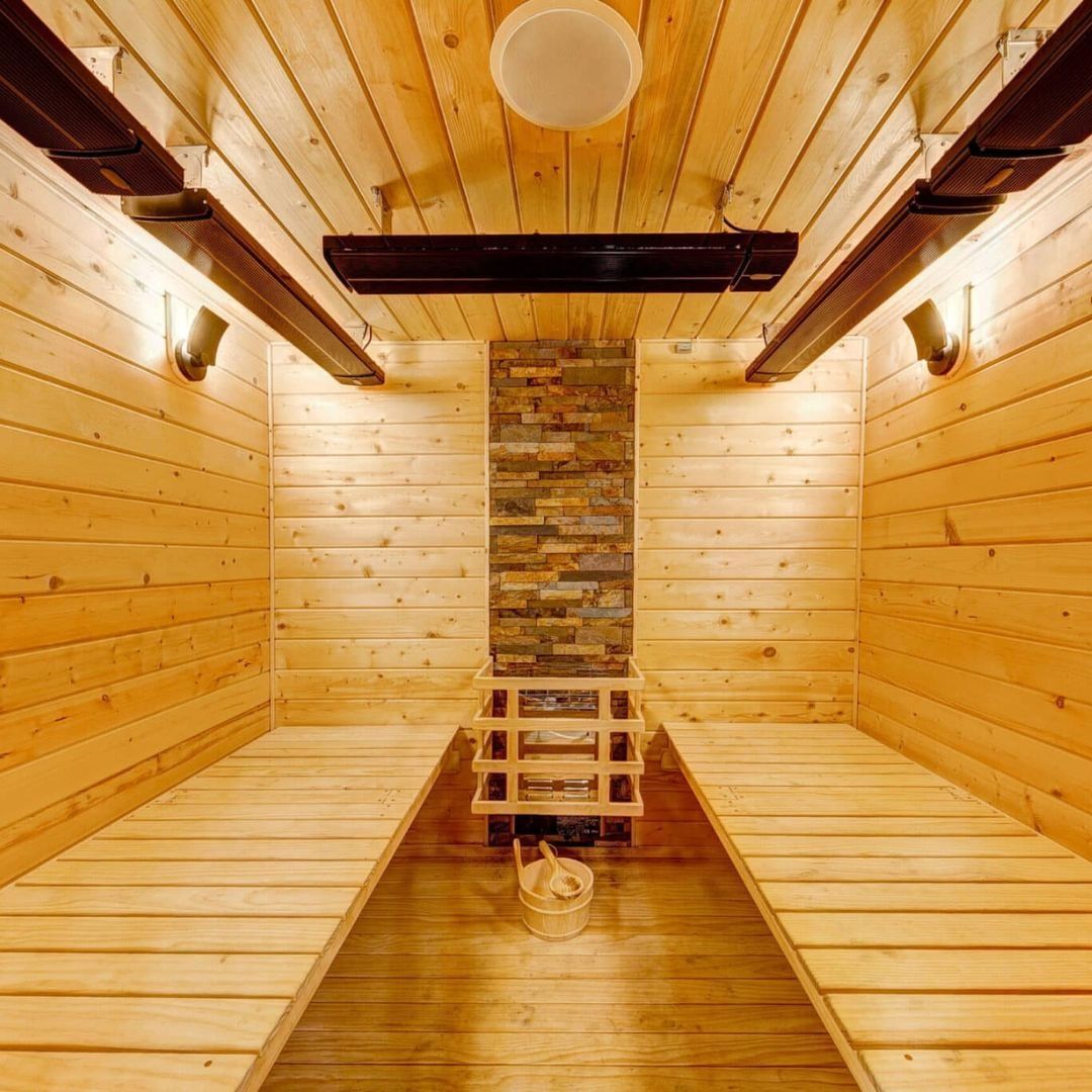 Interior view of a wooden sauna with benches, a small wooden ladder, and a stone wall feature.